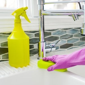 Hand scrubbing white sink with yellow sponge